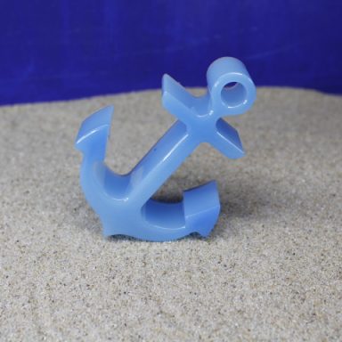 Blauer Anker aus Kunststoff auf sandfarbenem Untergrund.