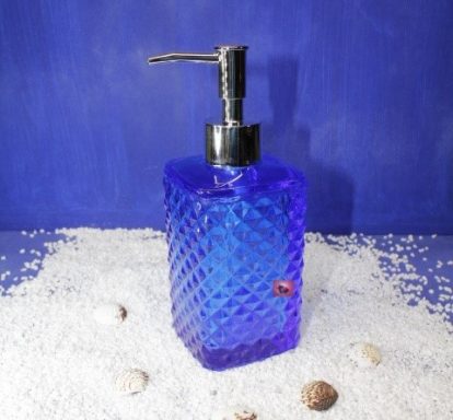 Blauer, quadratischer Seifenspender mit glänzendem Pumpmechanismus auf hellem Untergrund.