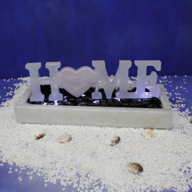 Dekoratives Element mit dem Wort "HOME", umgeben von weißen Kieselsteinen und Muscheln.