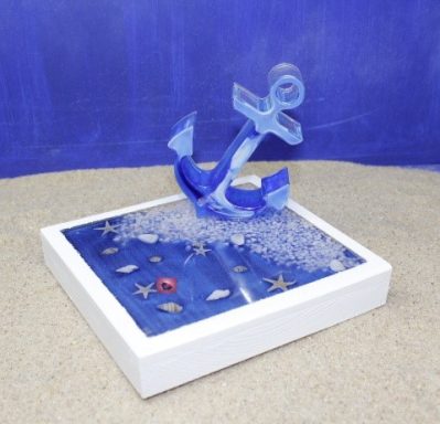 Ein blauer Anker steht in einem dekorativen Sandkasten mit Muscheln.