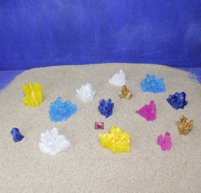 Bunte Kristalle in verschiedenen Formen auf hellem Sandhintergrund.
