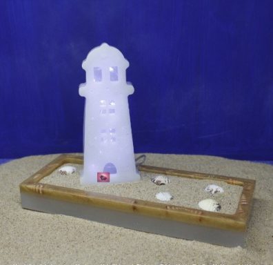 Leuchtturm aus Kunststoff auf Sand mit Muscheln in Schale.