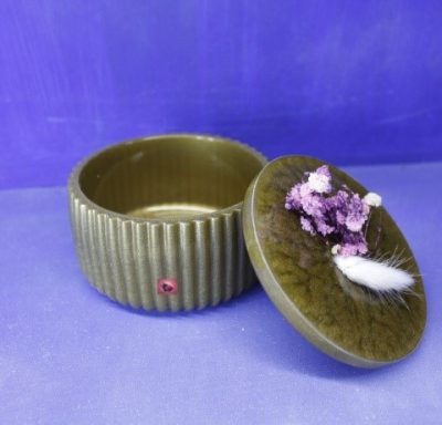 Runde, erdige Dose mit Reliefstruktur und Deckel, dekoriert mit lila Blüten.