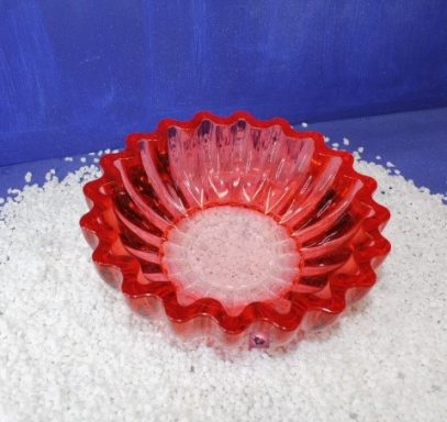 Rote, wellenförmige Schale auf einem weißen, glitzernden Untergrund.