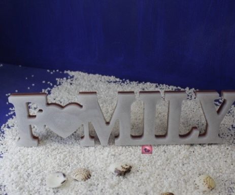 Holzschriftzug "FAMILY" mit Herz, umgeben von Muscheln und Sand.