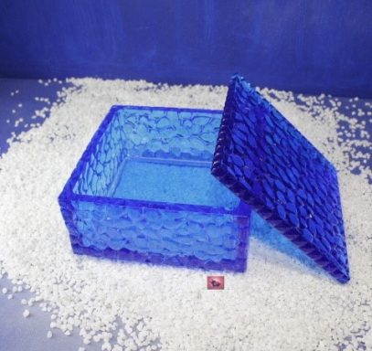 Blauer, quadratischer Behälter mit Deckel, umgeben von weißen Kügelchen.